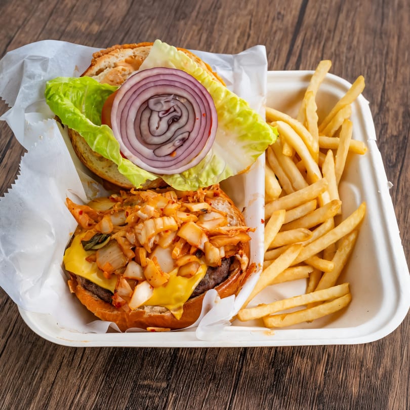 A kimchi burger with cheese, lettuce, and red onion, served with a side of french fries.