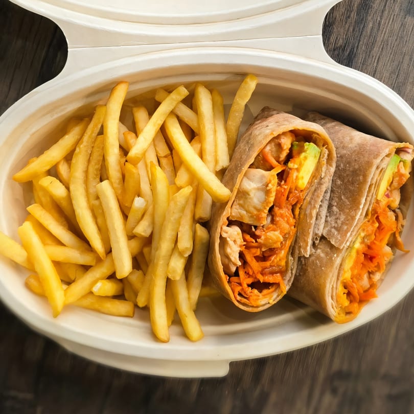 Two Korean chicken and avocado wraps with shredded carrots, served with golden french fries in a takeout container.