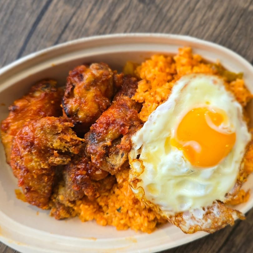Korean fried chicken with spicy sauce, orange fried rice, and a sunny-side-up egg in a bowl.